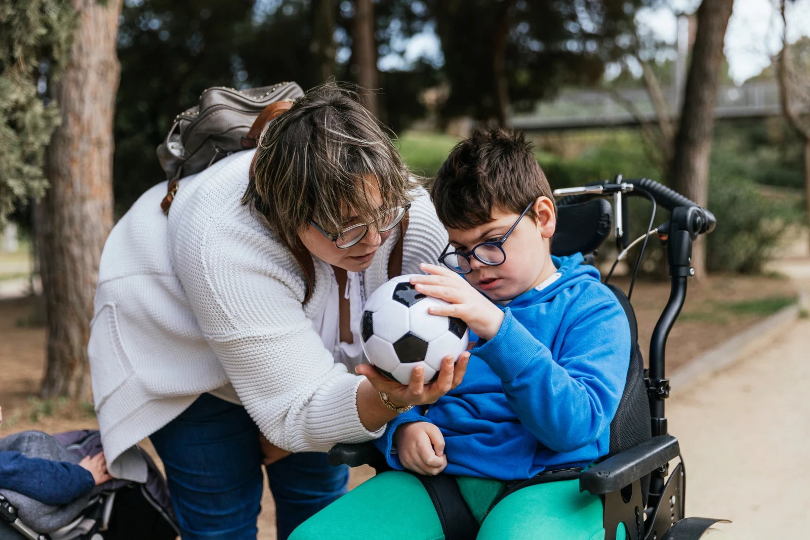 Child with multiple disabilities in a wheelchair playing with a soccer ball with her mother outdoors. Disabled people and childhood concept.